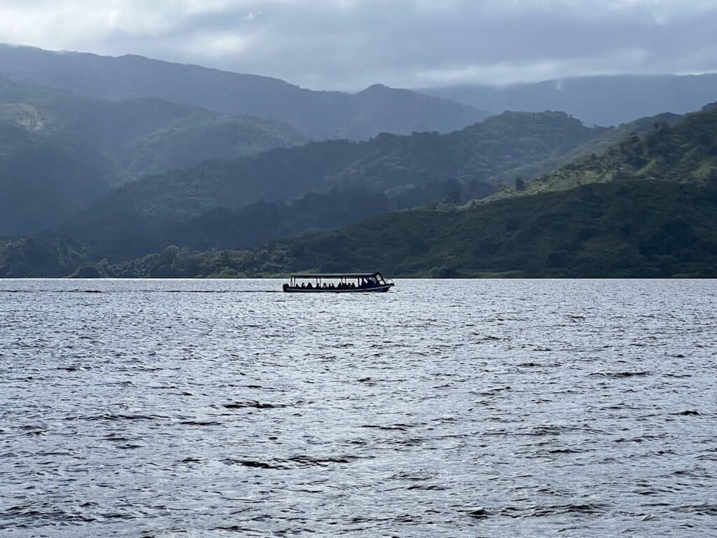 Small passenger boat crossing Lake Arenal beneath misty green hills, Costa Rica