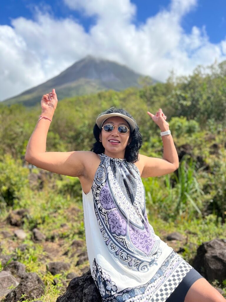 Milli with arms raised before a volcano in Costa Rica