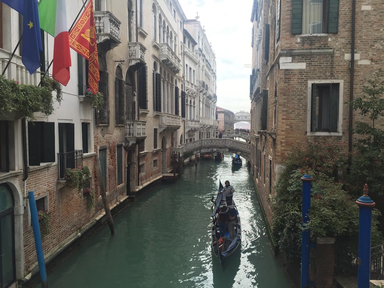A gondola on a narrow Venetian side canal seen from a bridge, with palazzi on both banks