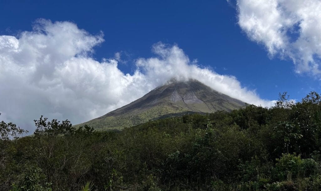 Arenal Volcano rising above rainforest under cloud, Costa Rica