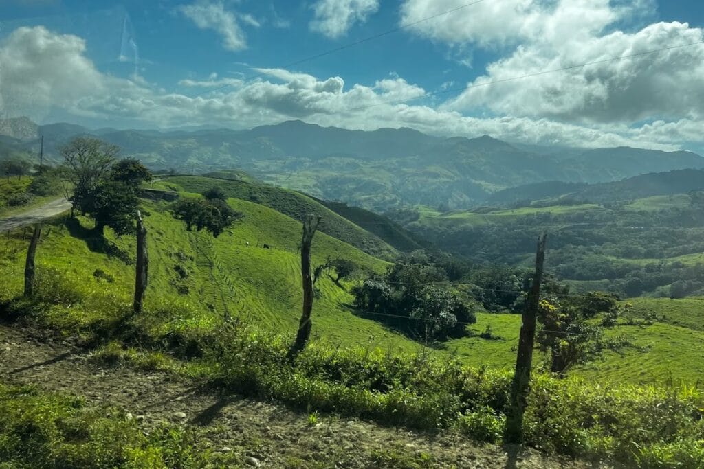 Rolling green pasture and distant mountains under a bright sky, Costa Rica highlands.