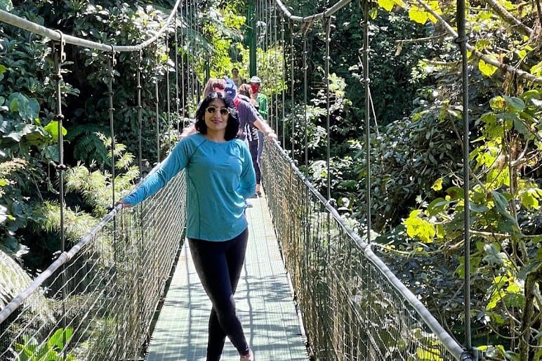 A person on a suspension footbridge through dense green cloud forest.