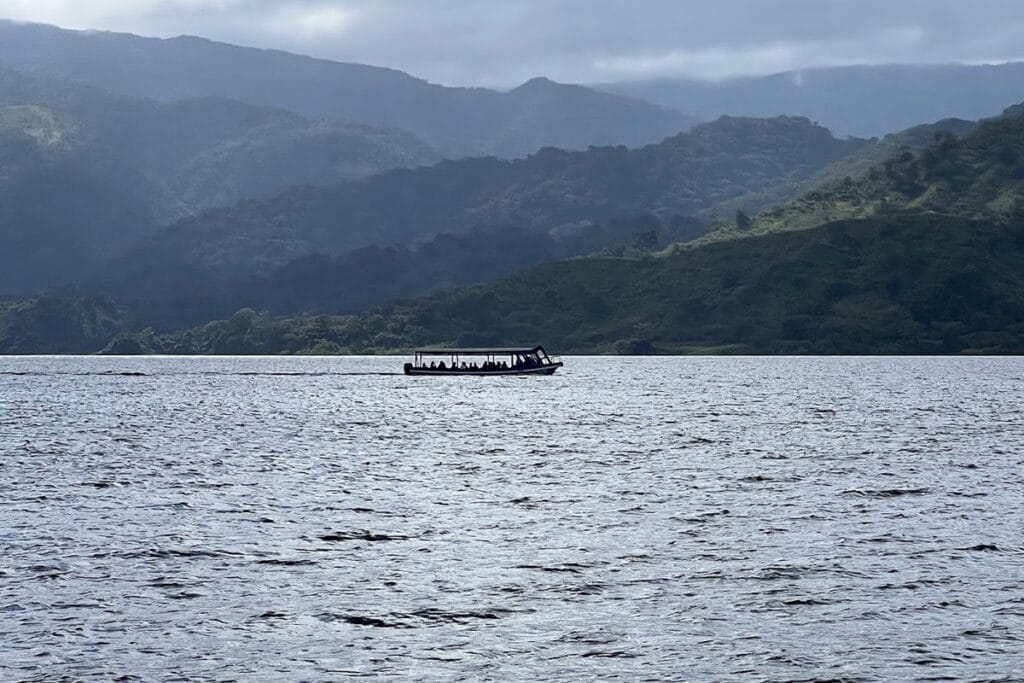 A small passenger boat on Lake Arenal with forested mountains beyond.