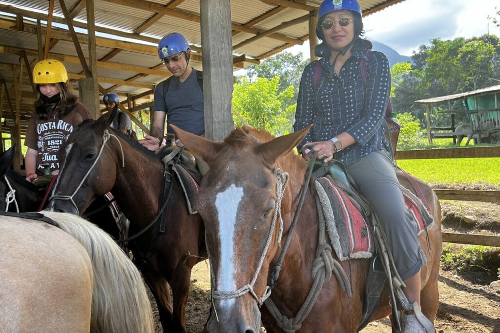 A rider on horseback at a countryside stable near Arenal, with more riders and green hills behind.