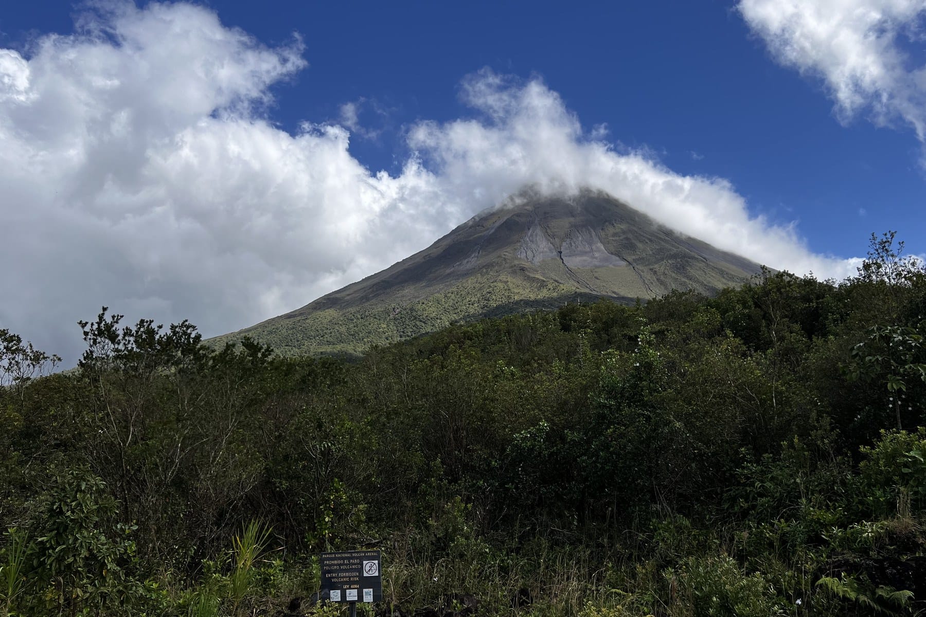 The conical Arenal Volcano rising above green forest under a bright sky, Costa Rica.