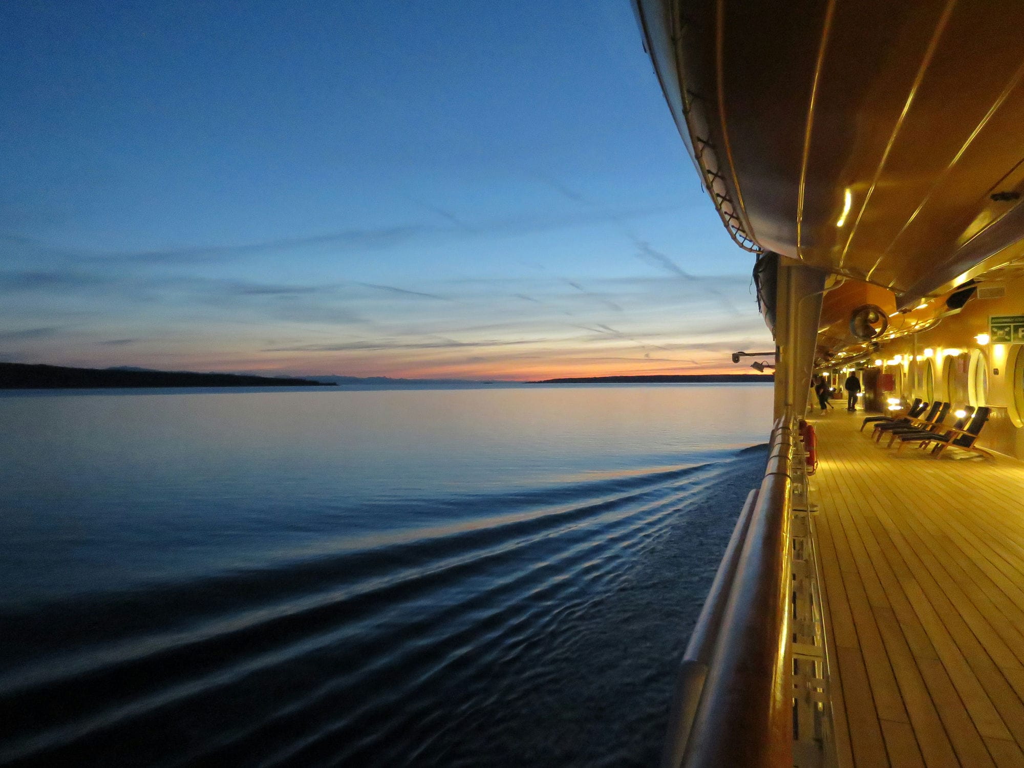 Warm evening light along the teak deck of a cruise ship as the sun sets over calm water