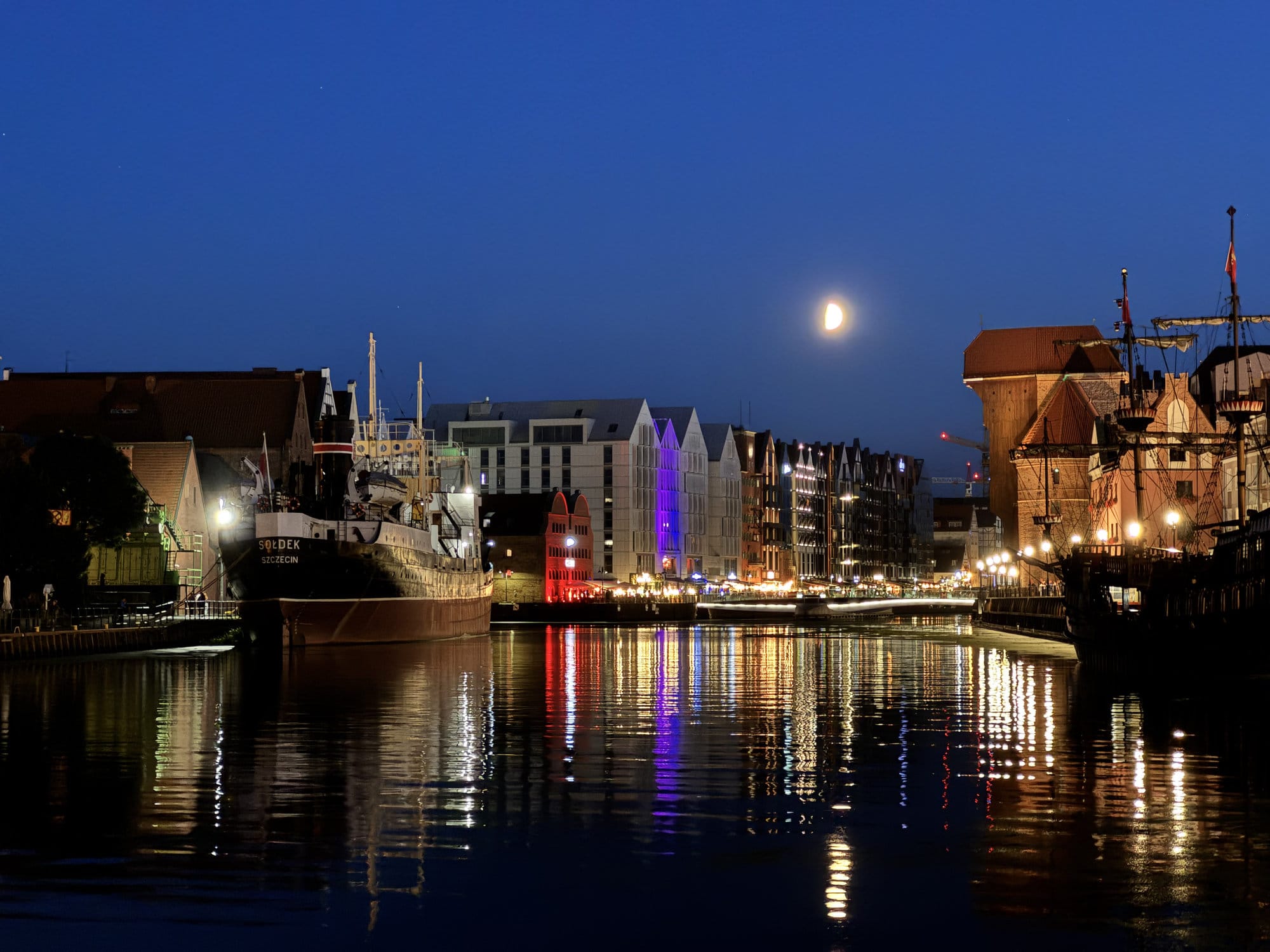 Moon over the Motława river in Gdańsk, the medieval Crane and lit quayside reflected in still water