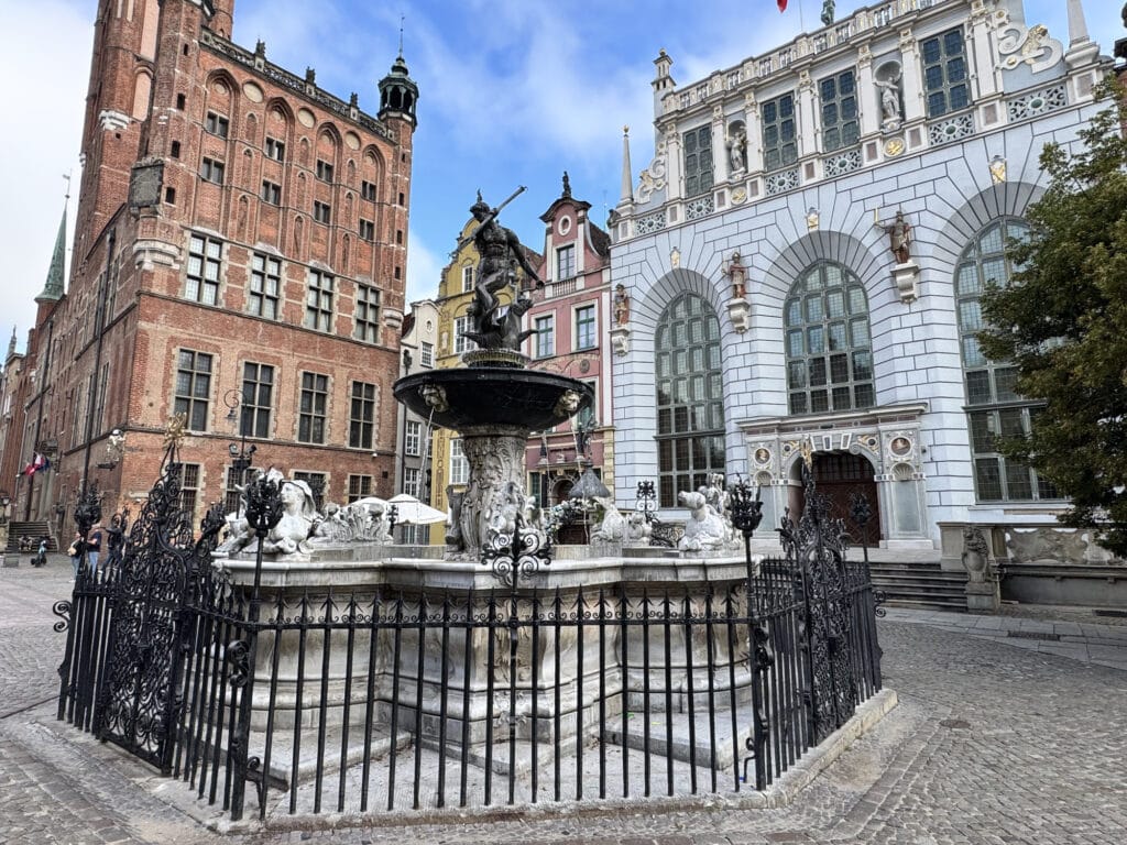 Neptune's Fountain behind its ironwork railing on Long Market in Gdańsk, with the facade of Artus Court and the Main Town Hall tower