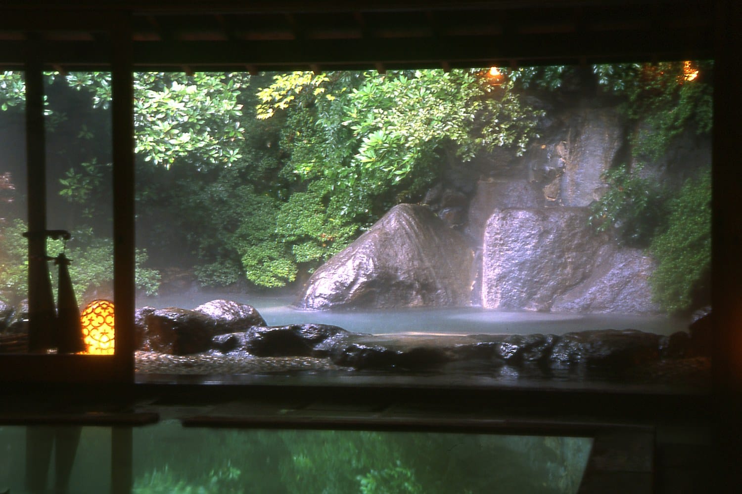 Japanese ryokan room with a round wooden hot-spring tub and a balcony over green forest.