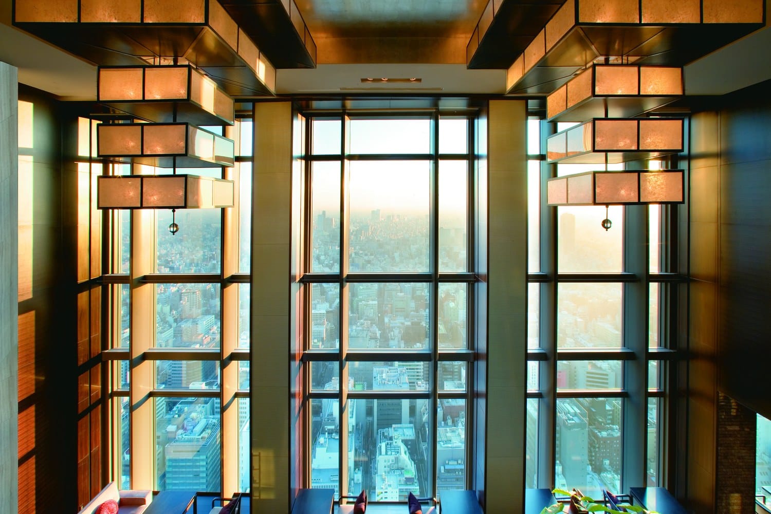 High-floor hotel lounge with tall lattice-framed windows overlooking the Tokyo skyline, warm lantern lighting.