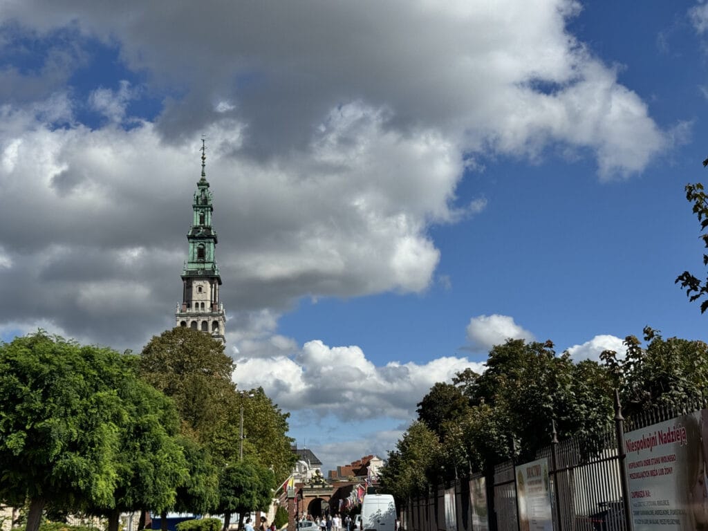 The baroque tower of the Jasna Góra monastery rising above trees in Częstochowa under broken cloud