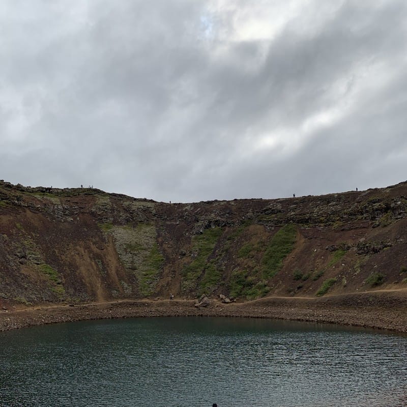 The blue-green crater lake inside Kerið volcanic crater in southwest Iceland, ringed by red volcanic rock