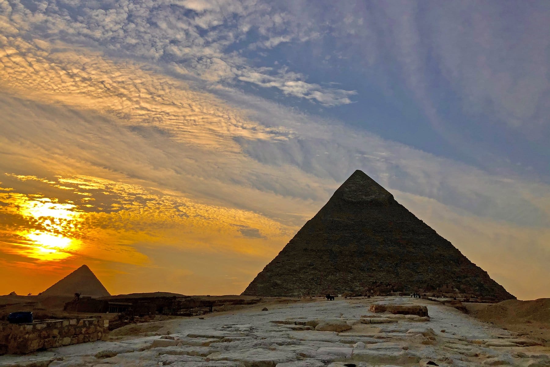 A pyramid at Giza silhouetted against a golden, cloud-streaked sunset sky