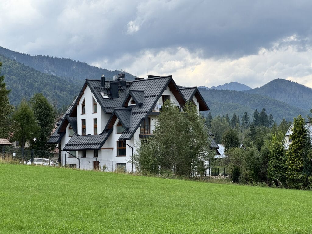 A steep-roofed highland house standing in a green meadow below forested Tatra ridges under storm cloud