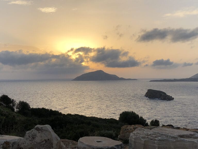 The ruined columns of the Temple of Poseidon at Cape Sounion silhouetted against the sunset over the sea.