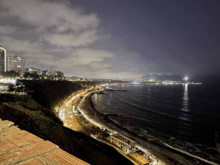 Night view over Miraflores in Lima, the lit coastal highway and beach curving along the Pacific with the city and headland lights beyond.