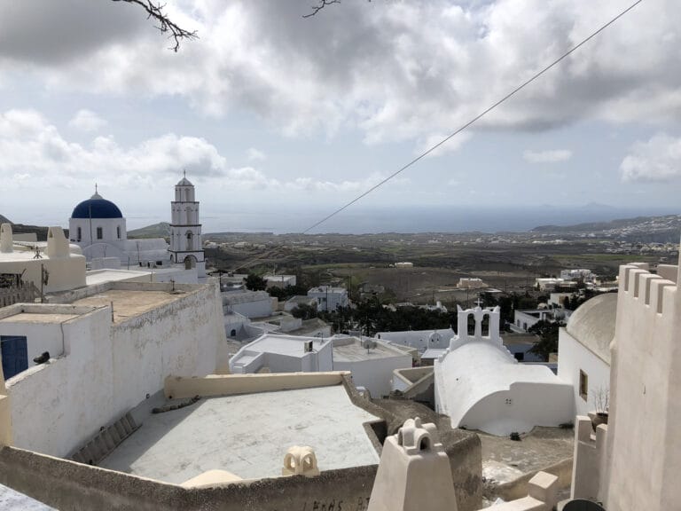 The hilltop village of Pyrgos Kallistis on Santorini, with a historic bell tower and a blue-domed church.